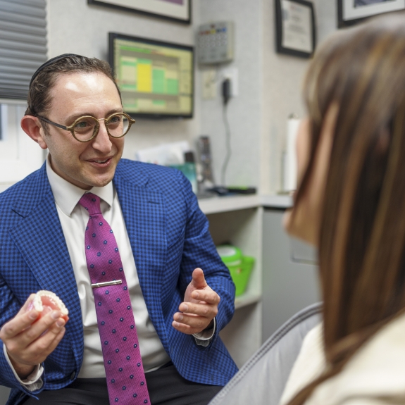 Doctor Ariel talking to a patient in the dental chair while holding a denture