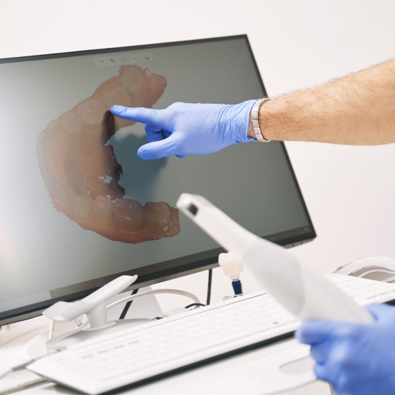 Dentist pointing to a screen showing a digital model of a row of a patients teeth