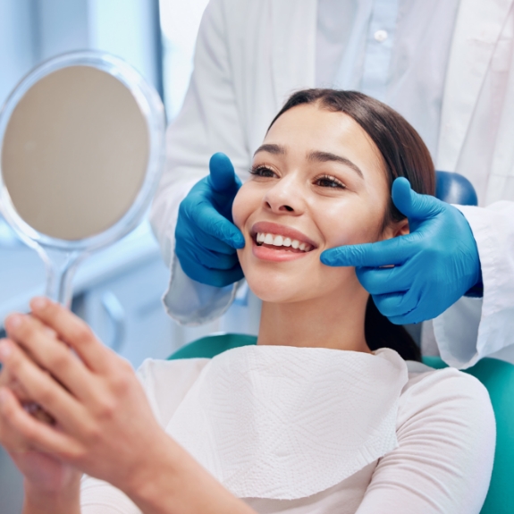Young woman in the dental chair admiring her new smile in a mirror