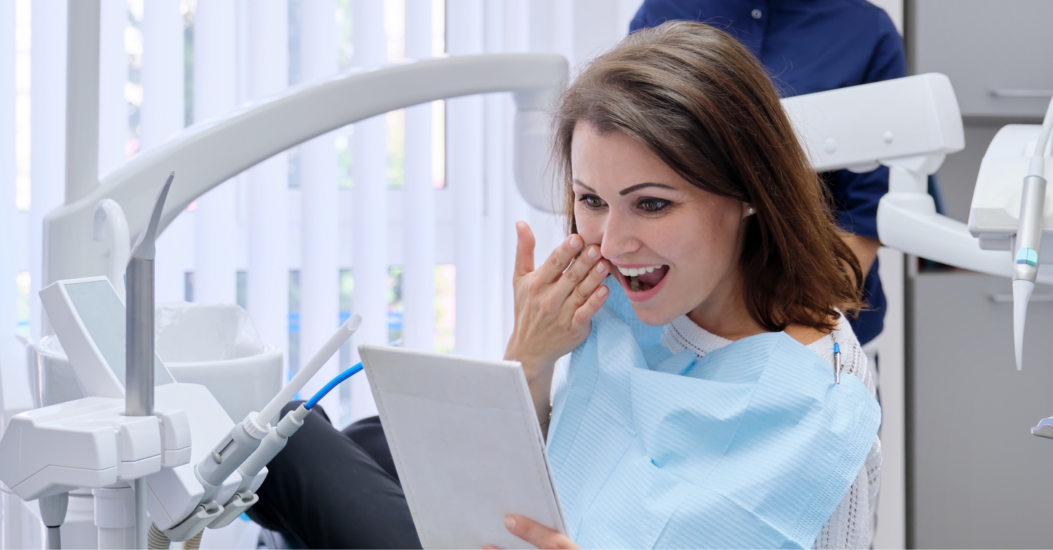 Dental patient admiring her smile in a mirror after getting dental bridges in Massapequa Park