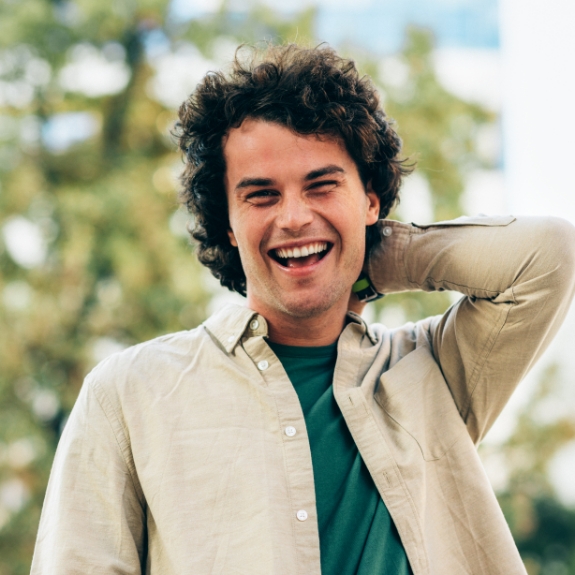 Young man with curly brown hair smiling outdoors