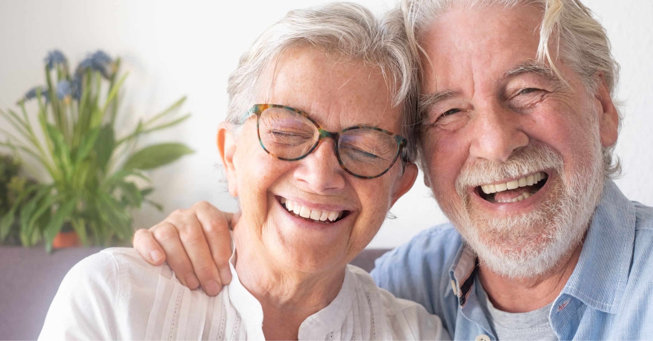 Older man and woman laughing together at home after seeing their dentist for seniors in Massapequa Park