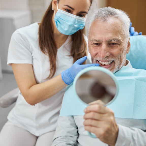 Senior dental patient looking at his new smile in a mirror