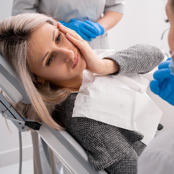 Woman holding her cheek in pain while visiting her emergency dentist