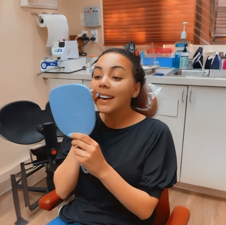 Young woman in the dental chair looking at her new smile in a mirror
