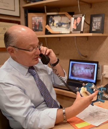 Doctor Mohr sitting at a desk and talking on the phone while holding a model of the mouth
