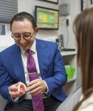 Doctor Ariel smiling while showing a patient a model of the teeth