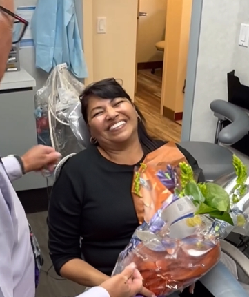 Woman in dental chair grinning and holding a flower bouquet
