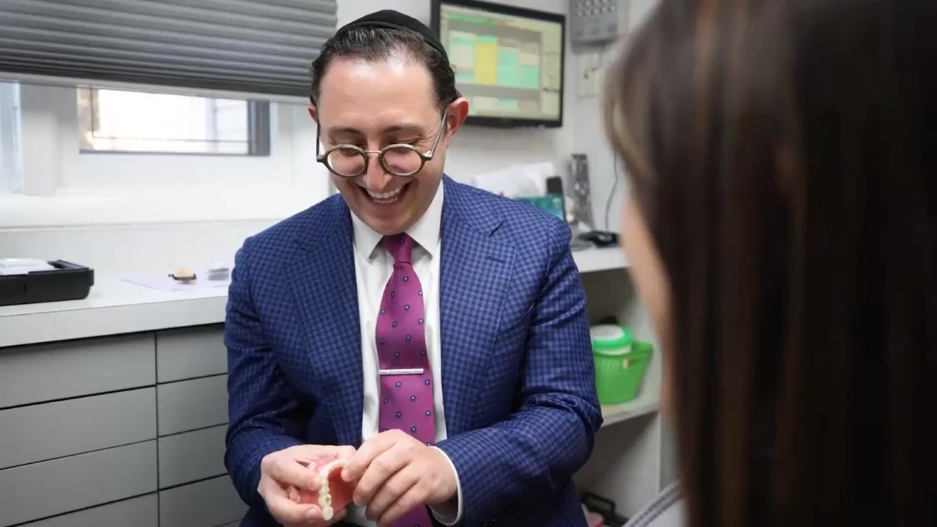 Doctor Ariel smiling while showing a denture to a patient
