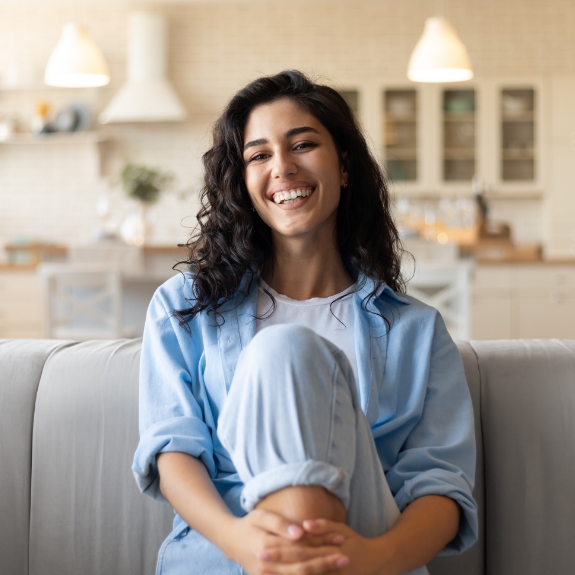 Woman in a light blue jacket smiling on her couch