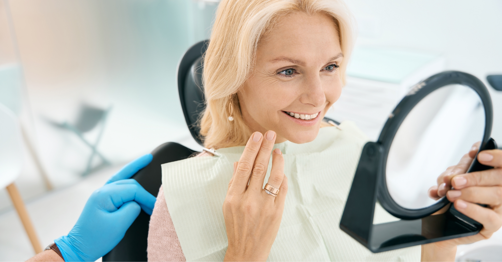 Woman in the dental char looking at her teeth in a mirror after a smile makeover in Massapequa Park