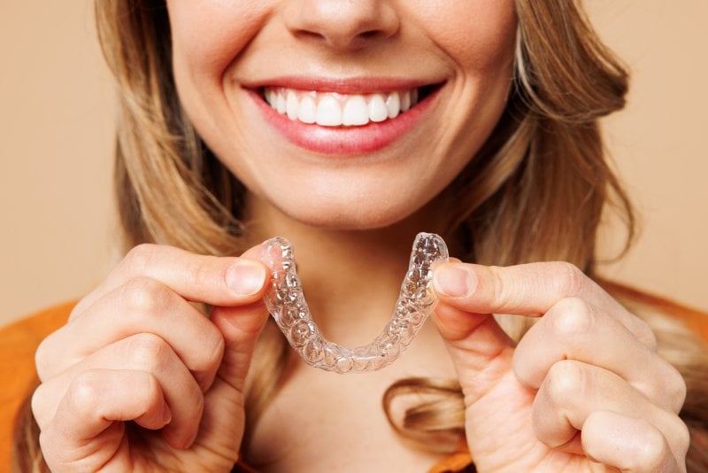smiling woman holding Invisalign tray 