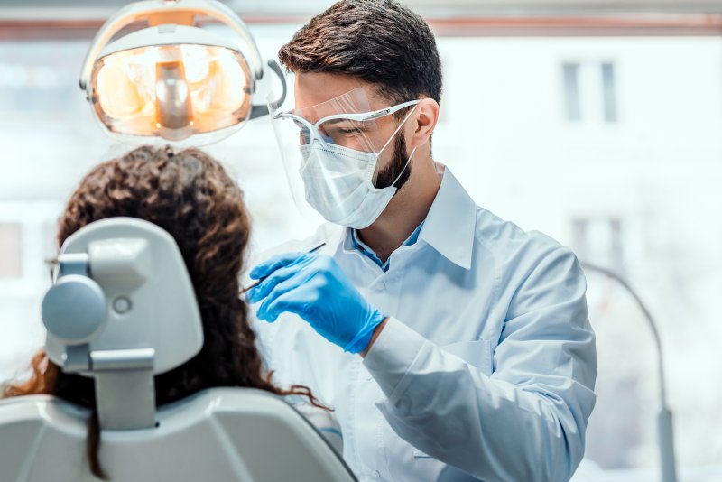 a male dentist wearing personal protective equipment while caring for a patient’s smile