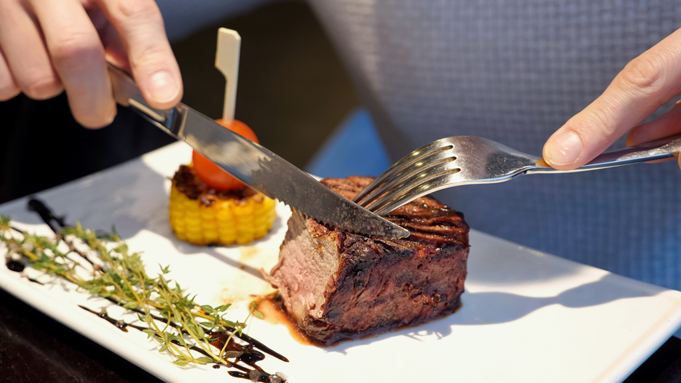 man with dentures cutting steak into small bites 
